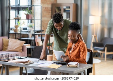 Smiling Young African American Couple Using Tablet App While Planning Family Budget In Living Room