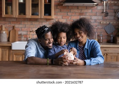 Smiling Young African American Family With Daughter Save Money In Piggybank Feel Provident Economical About Finances. Happy Biracial Parents With Ethnic Child Make Financial Investment For Future.