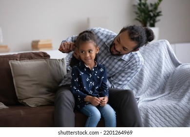 Smiling young African American father detangling long curly hair of cute happy little preteen child daughter, making hairstyle helping getting ready for school, sitting together on couch at home. - Powered by Shutterstock