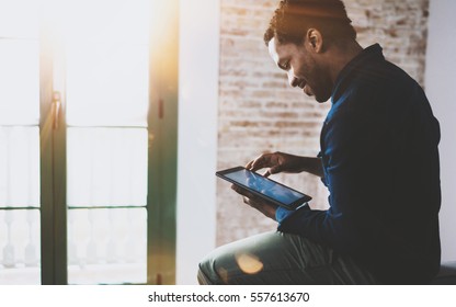 Smiling Young African American Freelancer Touching Screen Digital Tablet While Working In New Project At Home.Black Businessman Looking For Information On Internet.Blurred,color Filter,flares