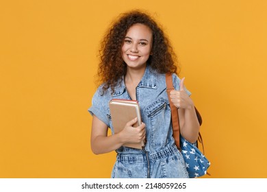 Smiling young african american girl student in denim clothes, backpack isolated on yellow background studio portrait. Education in high school university college concept. Hold books, showing thumb up