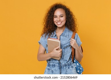 Smiling young african american girl student in denim clothes backpack isolated on yellow background studio portrait. Education in high school university college concept. Hold books, looking camera