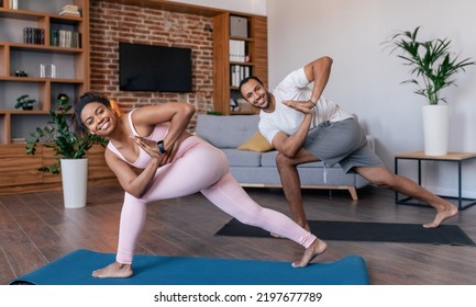 Smiling Young African American Male And Female In Sportswear Doing Exercises For Legs Or Practicing Yoga In Living Room Interior, Panorama. Body Care Together, Weight Loss, Fit At Home During Covid-19