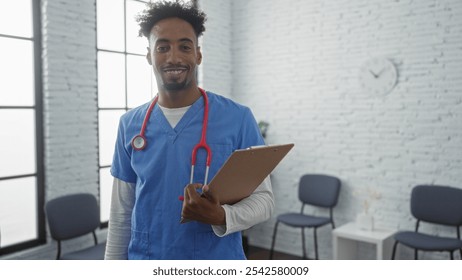 Smiling young african american male doctor in blue scrubs with a red stethoscope holding a clipboard in a modern clinic waiting room. - Powered by Shutterstock