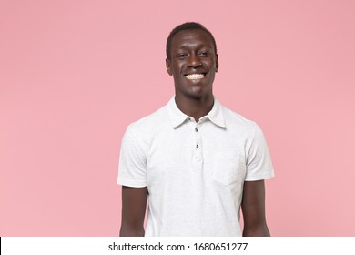 Smiling Young African American Man Guy In White Polo Shirt Posing Isolated On Pastel Pink Background Studio Portrait. People Sincere Emotions Lifestyle Concept. Mock Up Copy Space. Looking Camera