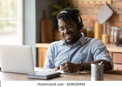 Smiling young African American man in headphones glasses make note watching webinar on laptop. Happy male in earphones work take online course distant training on computer at home. - Shutterstock ID 1838100496