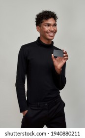 Smiling Young African American Man Holding Credit Card Mockup And Looking To Side While Posing On Light Background, Vertical Shot. Discount And Sale Concept