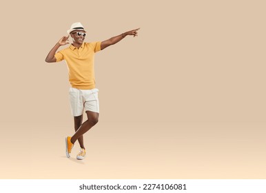 Smiling young African American man in casual summer wear and sunglasses pose on brown studio background point at empty copy space. Happy biracial guy show good deal or sale offer. - Shutterstock ID 2274106081