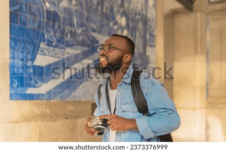Smiling young african american man with cmera against classical azulejo wall. Travel in Portugal