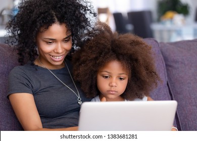 Smiling Young African American Mom Relax With Small Daughter On Couch At Home With Laptop Watching Cartoons Online, Millennial Black Mommy Rest With Little Child, Teach Her Using Computer