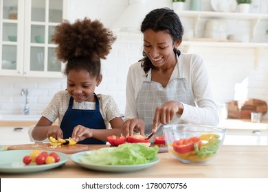 Smiling young african American mother and small daughter chop vegetables prepare healthy vegetarian salad in kitchen, happy biracial mom teach little girl child cooking food at home, dieting concept - Shutterstock ID 1780070756