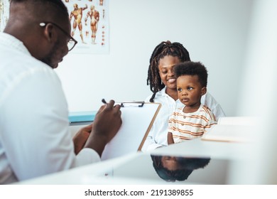 Smiling Young African American Mother With Small 2s Boy Child Son Have Consultation With Caring Male Pediatrician In Private Hospital Or Clinic. Attentive Male Doctor Support Cheer Little Kid Patient.