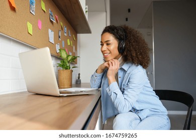Smiling young african american teen girl wear headphones video calling on laptop. Happy mixed race pretty woman student looking at computer screen watching webinar or doing video chat by webcam. - Shutterstock ID 1674759265