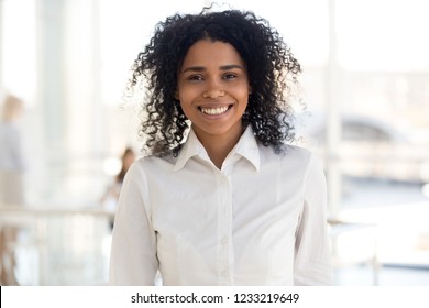 Smiling Young African American Woman Employee, Intern Girl, Worker Or Student Looking At Camera In Modern Office, Happy Millennial Mixed Race Black Professional, Business Coach Headshot Portrait