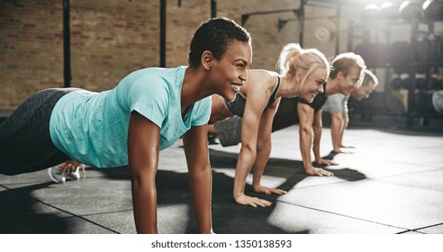 Smiling young African American woman in sportswear doing pushups during an exercise class with a group of friends at the gym