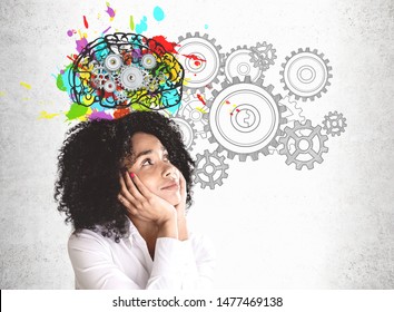 Smiling Young African American Woman In White Shirt Looking At Colorful Brain Sketch With Gears Drawn On Concrete Wall. Concept Of Brainstorming