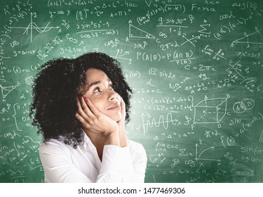 Smiling young African American woman in white shirt looking at blackboard with formulas. Concept of education and science - Powered by Shutterstock