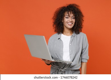 Smiling Young African American Woman Girl In Gray Casual Clothes Isolated On Orange Wall Background Studio Portrait. People Lifestyle Concept. Mock Up Copy Space. Working On Laptop Pc Computer