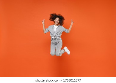 Smiling young african american woman girl in gray casual clothes posing isolated on orange wall background studio portrait. People lifestyle concept. Mock up copy space. Jumping, showing victory sign
