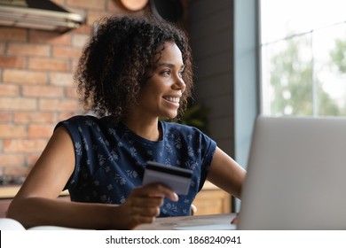 Smiling young african american woman holding plastic bank card in hands, planning products purchase in internet store, looking in distance, dreaming of sale season, planning buying gifts online. - Powered by Shutterstock