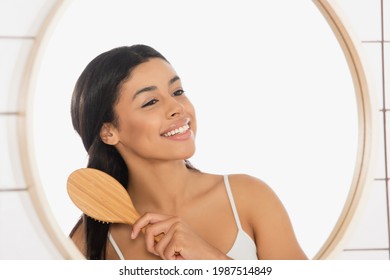 Smiling Young African American Woman Brushing Hair Near Mirror In Bathroom