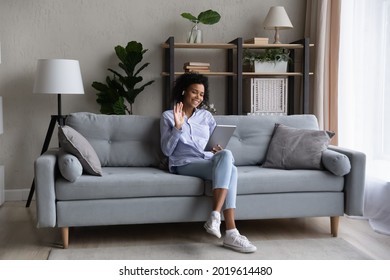 Smiling young African American woman sit on sofa at home wave greet talking speaking on video call on pad. Happy biracial female have webcam digital virtual event on tablet. Communication concept. - Powered by Shutterstock