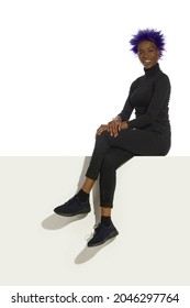 Smiling young african american woman in black clothes is sitting on a top of a white banner. Full length studio shot. - Shutterstock ID 2046297764