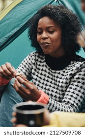 Smiling Young African American Woman Eating A Meal During A Camping Trip With Friends In A Forest