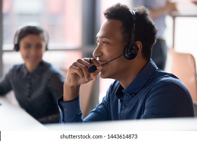 Smiling young african businessman call center agent wear wireless headset laugh at workplace, cheerful happy black male telemarketer operator have fun at work break in customer service support office