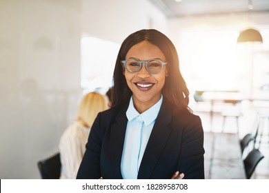 Smiling young African businesswoman standing in an office boardroom with colleagues working at a table in the background