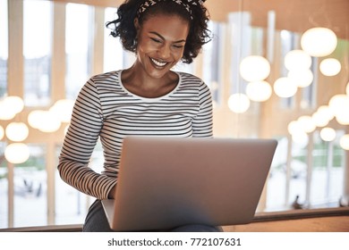 Smiling young African college student sitting on the floor in a campus hallway working online with a laptop between classes