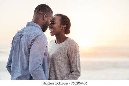 Smiling young African couple talking and laughing together while standing face to face on a beach at sunset