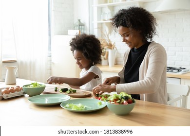 Smiling Young African Ethnicity Woman Giving Culinary Educational Class To Curious Small Biracial Child Daughter, Chopping Fresh Vegetables Together At Countertop In Kitchen, Diverse Family Cooking.