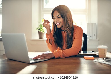 Smiling Young African Female Entrepreneur Sitting At A Table In Her Home Office Working On A Laptop