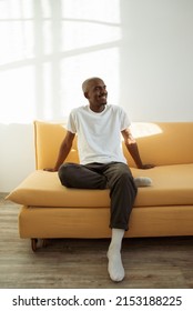 Smiling Young African Man Relaxing At Home On The Yellow Couch In A Room Lit With Sunshine