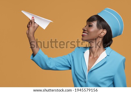 Smiling young african stewardess holding a paper airplane in her hand. Orange background.