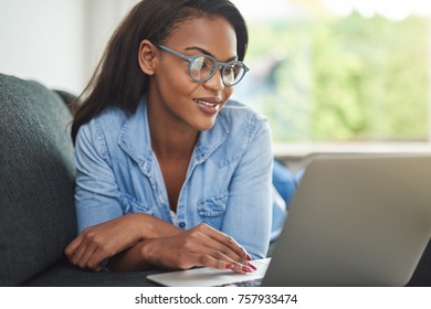 Smiling young African woman browsing online with a laptop while lying down on her living room sofa at home - Shutterstock ID 757933474