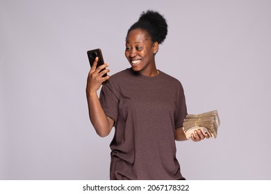 Smiling Young African Woman Holding A Lot Of Money And Using Her Phone