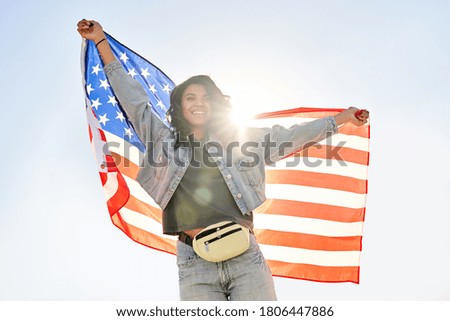 Smiling young African woman holding usa flag dancing under sunny sky looking at camera. Happy free independent patriot Afro American lady waving United States flag dancing outdoor feeling freedom.