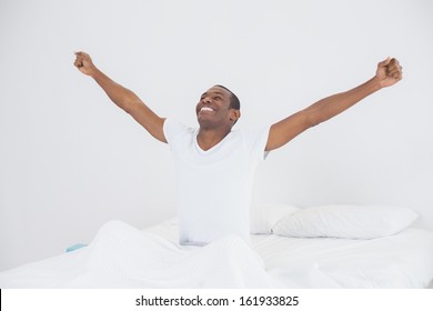 Smiling Young Afro Man Stretching His Arms Out In Bed At Home