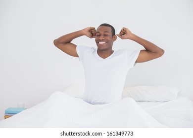Smiling young Afro man waking up in bed and stretching his arms