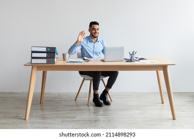 Smiling Young Arab Business Man Making Video Call Using Laptop At Office, Having Web Conference Waving Hand At Computer Web Camera And Talking. Online Communication And Remote Work Concept