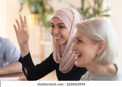 Smiling Young Arabian Woman Raise Hand Ask Or Answer Question Participate In Team Discussion At Meeting, Happy Arabic Female Employee Take Part In Group Brainstorming, Leadership Concept