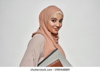 Smiling young arabic businesswoman in hijab with notepad looking at camera on light background while standing sideways. Beautiful muslim lady