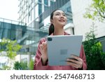 Smiling young Asian business woman holding tablet standing on the steps against on backdrop of business centers.leader entrepreneur,business woman holding digital tablet computer standing in city