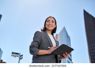 Smiling young Asian business woman leader entrepreneur  professional manager holding digital tablet computer using software applications standing the street in big city sky background 