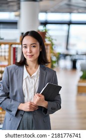 Smiling Young Asian Business Woman Wearing Suit Holding Digital Tablet Standing In Office. Professional Executive Manager Or Teacher Using Corporate Technology Looking At Camera. Vertical Portrait