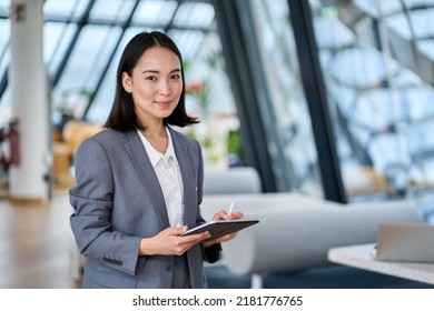 Smiling young Asian business woman leader holding digital tablet standing in office. Professional executive manager or saleswoman using corporate technology looking at camera. Portrait