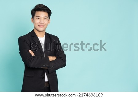 Smiling young Asian businessman with arms crossed isolated on green background