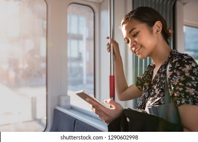 Smiling young Asian businesswoman catching up on social media while riding on a train in the city during her morning commute - Powered by Shutterstock